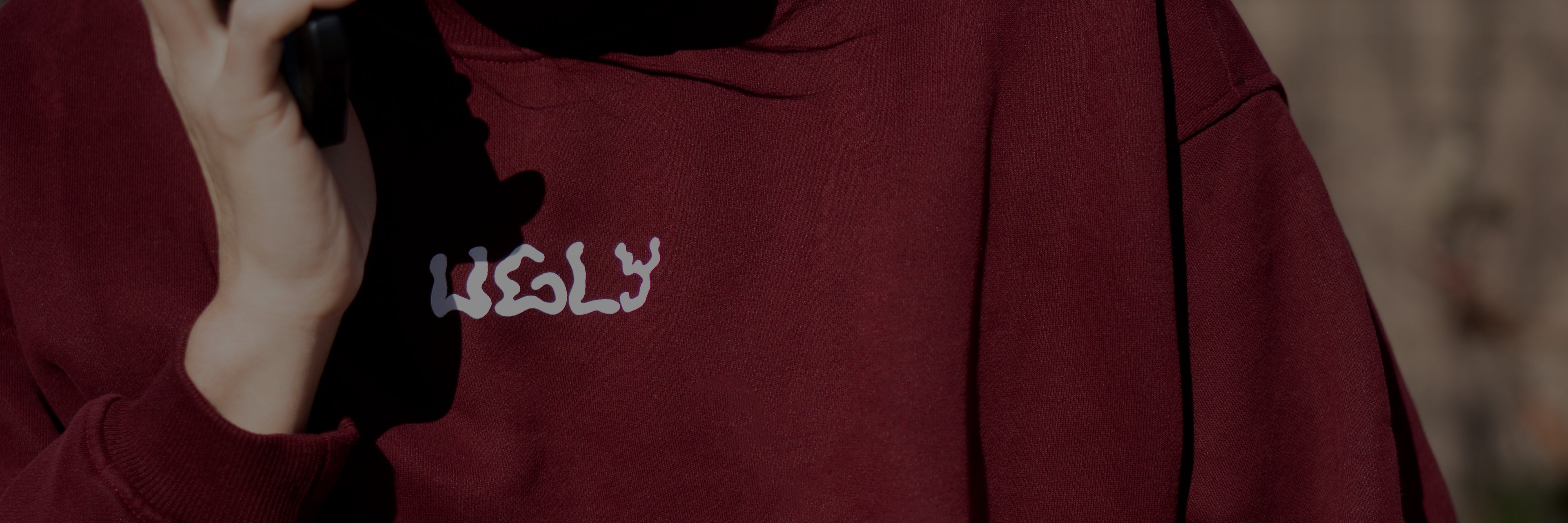 Maroon hoodie with 'UGLY' logo worn by a person, blurred background